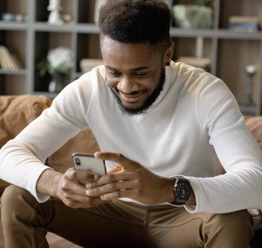 A man smiling as he texts on his phone.