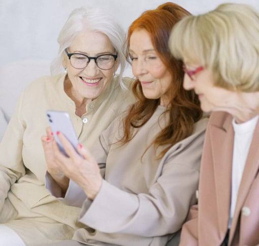 Three women laughing together at a video chat on a phone.